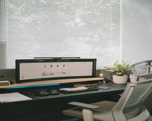 A clean workspace table setup near a window showing ergonomic monitor heights and comfortable chair placement